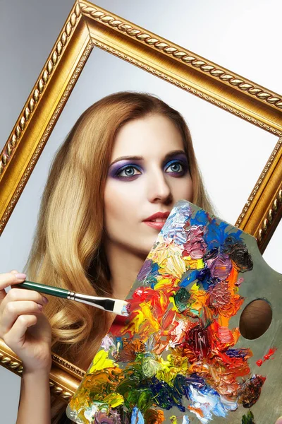 Young woman painter in golden frame with color pallet and paint