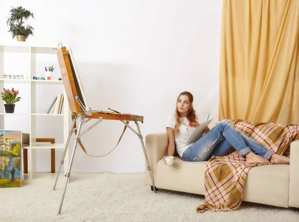 Painter female with wooden sketchbook sitting on sofa and painti