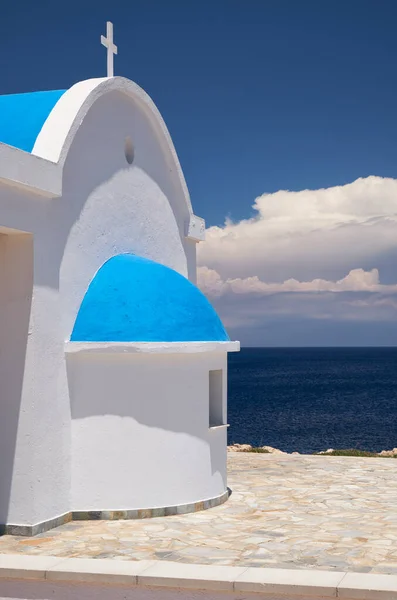 The view of the white chapel of Agioi Anargyroi on the rocky shore of Cape Greko (Cape Greco) against the vivid blue background of the Mediterranean water and sky. Cyprus