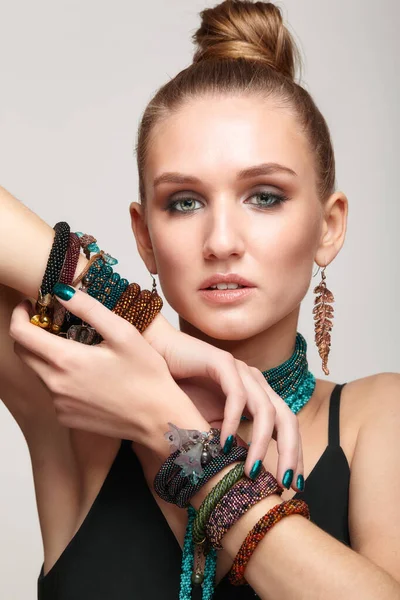 Beauty portrait of young female with hand up on gray background. Beautiful woman in collar necklace and multiple bracelets on hands.