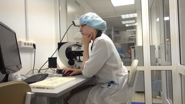 Mujer investigadora sentada a la mesa con microscopio — Vídeo de stock