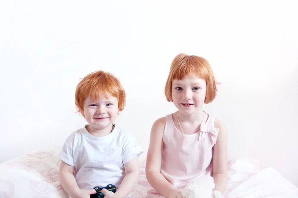 Red-haired brother and sister are sitting on the bed