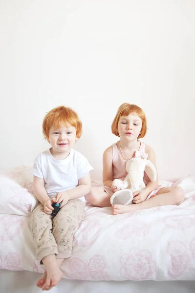 Red-haired brother and sister are sitting on the bed