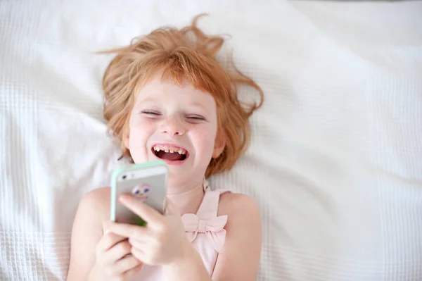 Red-haired girl with tooth decay laughs looking at the phone