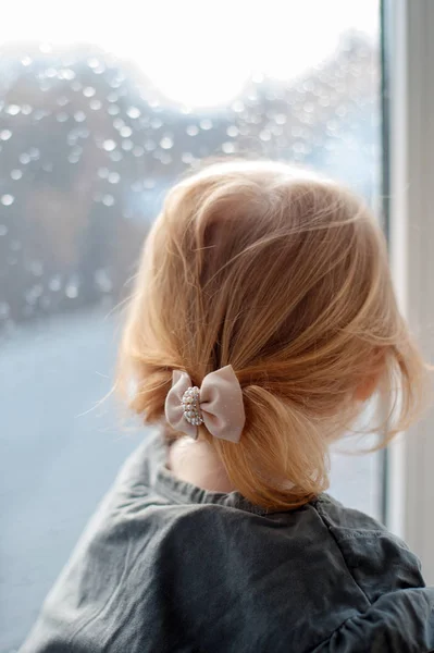 A girl sits on a window sill and looks out the window