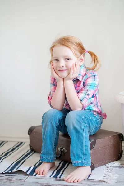 Ein Mädchen Jeans Und Kariertem Hemd Sitzt Auf Einem Koffer lizenzfreie Stockbilder