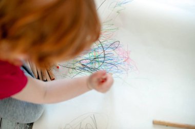 Çocuk kağıda renkli kalemler ile çizer.