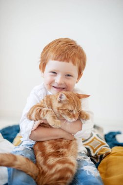 Kırmızı kedili, beyaz yataktaki komik kızıl saçlı çocuk.