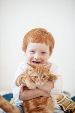 Kırmızı kedili, beyaz yataktaki komik kızıl saçlı çocuk.