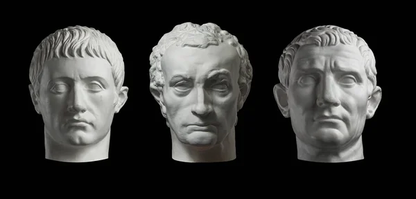 Trzy gipsowe kopie starożytnych głów posągów odizolowanych na czarnym tle. Tynk rzeźbiarskie twarze mężczyzn. — Zdjęcie stockowe
