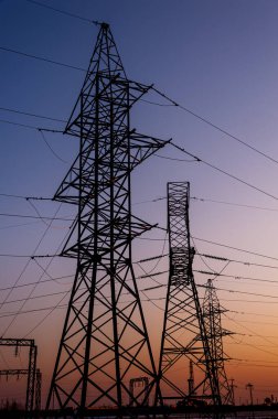 Elektrik direği, arka planda günbatımı kabloları var. İletişim kulesi. Renkli bir günbatımında elektrik hatları. Yüksek voltajlı elektrik hatlarını kapatın. Yüksek voltajlı elektrik iletim kulesi.