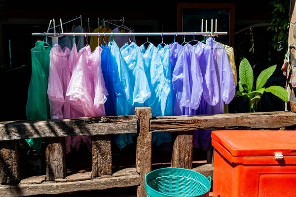 Someone selling safety vests and raincoat at local market. Thailands traditional street store. Rain protection. Multi-colored transparent waterproof raincoats hang in a row on a hanger.