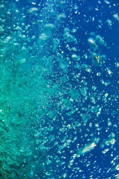 A close view at the coral reef sunlit. Air bubbles emitted by a diver who hidden under the deep dark ocean blue water column.Male in flippers examines the seabed.Floating fish looking for food. — Stock Photo, Image