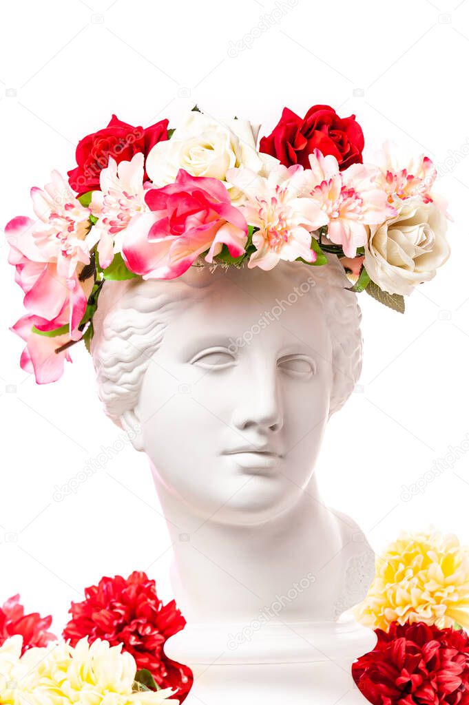 Beautiful young female white face and colorful flowers. Plaster antique bust of Venus in a floral wreath. Beauty spring and summer model girl with fresh bouquet.