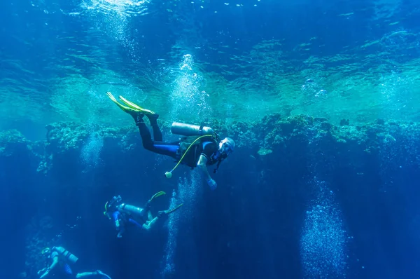 Vooraanzicht op duikers groep zwemmen die diep donker oceaan blauw water verkennen tegen de achtergrond van een koraalrif. Man en vrouw in zwemvliezen onderzoeken de zeebodem. Duiken. Actieve levensduur.Luchtbellen. — Stockfoto