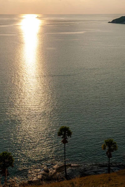 Vista su palme e isole vicino all'acqua di mare durante il bellissimo tramonto con un sole giallo brillante che splende sulle rocce. Adatto per uno sfondo carta da parati con un cielo giallo morbido. Sole sull'acqua . — Foto Stock
