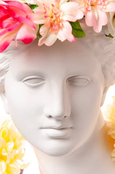 Beautiful young female face and colorful flowers. Plaster antique bust of Venus in a floral wreath. Beauty spring and summer model girl with fresh bouquet. — Stock Photo, Image