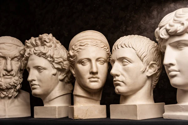 Group gypsum busts of ancient statues human heads for artists on a dark background. Plaster sculptures of antique people faces. Renaissance epoch style. Academic subject. Blank for creativity. — Stock Photo, Image