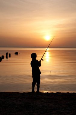 Silhouette of a boy fisherman on a sunset background