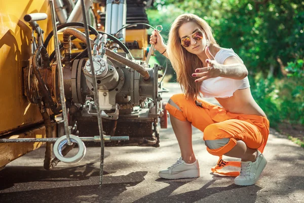 Sexy mulher trabalhador está reparando tratores motor com a chave . — Fotografia de Stock