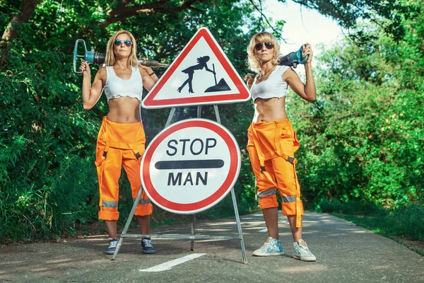 Twee sexy vrouwen werknemers in overall met de pneumatische boren. — Stockfoto