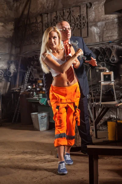 Blonde vrouw is zijn baas met de moersleutel straffen. Workshop over de achtergrond. — Stockfoto