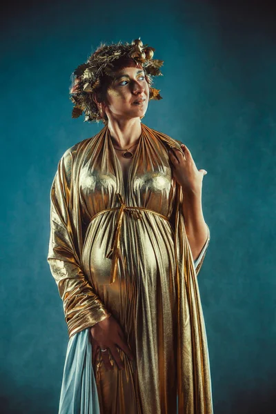 Mulher grávida em toga dourada e grinalda posando como uma deusa da fertilidade da Grécia — Fotografia de Stock