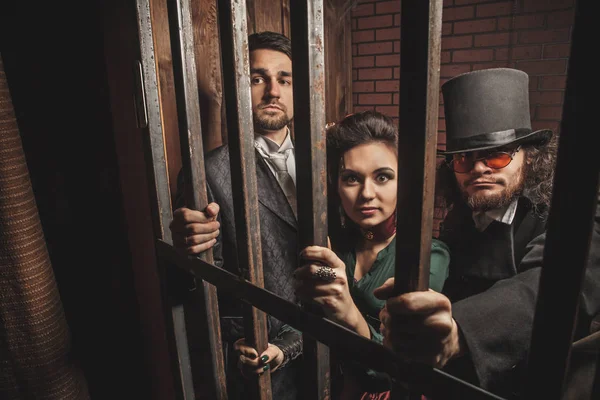 Two gentlemen and a lady behind bars in the prison. — Stock Photo, Image