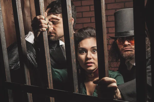 Two gentlemen and a lady behind bars in the prison. — Stock Photo, Image