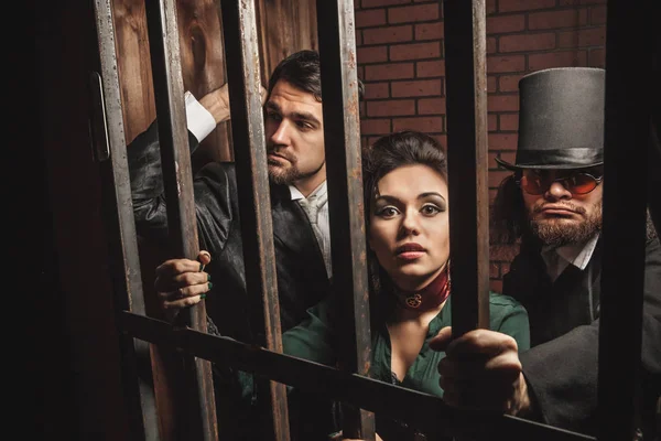 Two gentlemen and a lady behind bars in the prison. — Stock Photo, Image