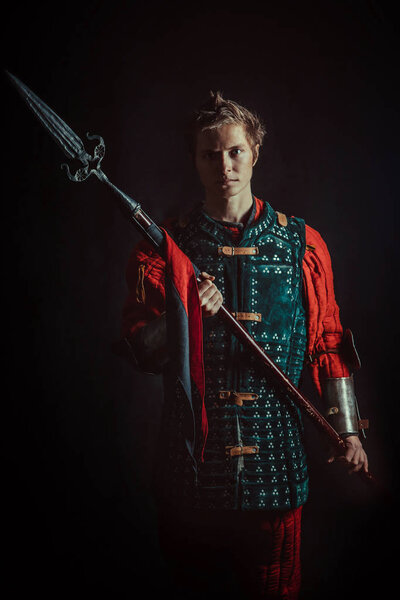 Young medieval warrior with the spear. Dark background.