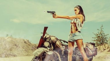 Seksi motorcu kadın motosiklet çöl arka plan üzerinde yakınındaki silahla.