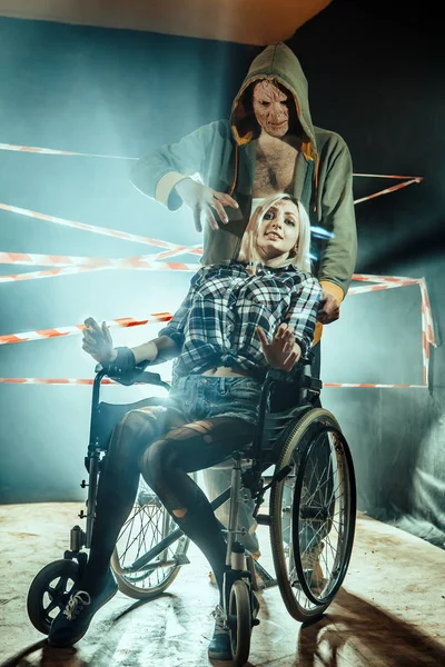 Маньяк и его связанная жертва в инвалидной коляске на темном фоне . — стоковое фото