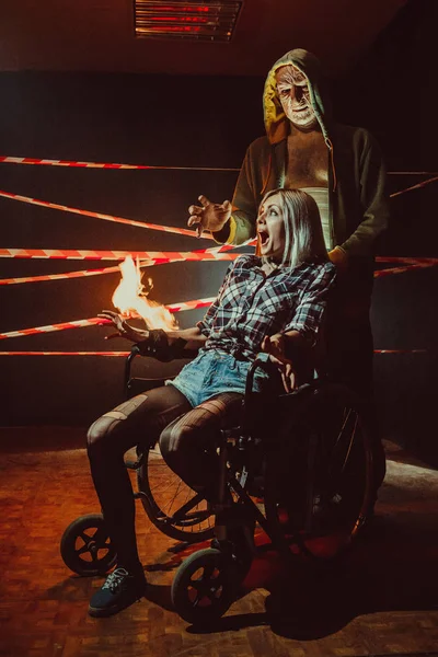 Maniac e sua vítima amarrada na cadeira de rodas no fundo escuro . — Fotografia de Stock