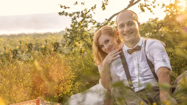 Casal atraente desfrutando de piquenique romântico ao pôr do sol no campo — Fotografia de Stock