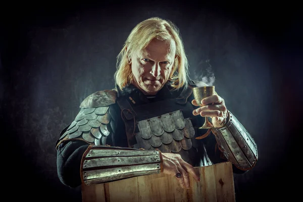 Powerful blond knight with the glass of wine on the dark background. — Stock Photo, Image