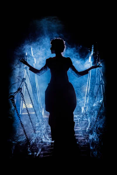 Silhouette einer geheimnisvollen Hexe, die den Zauber spricht und uns ihre Hände ausstreckt, mit Rauchwolken um sie herum und einer Dungeonbrücke im Hintergrund — Stockfoto