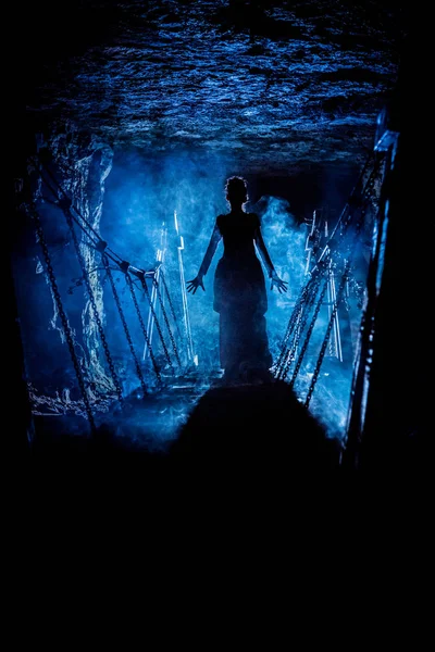 Σιλουέτα της μια μυστηριώδης μάγισσα λέγοντας το ξόρκι και τεντώνοντας τα χέρια της σε μας, με σύννεφα καπνού γύρω της, και dungeon γέφυρα στο φόντο — Φωτογραφία Αρχείου