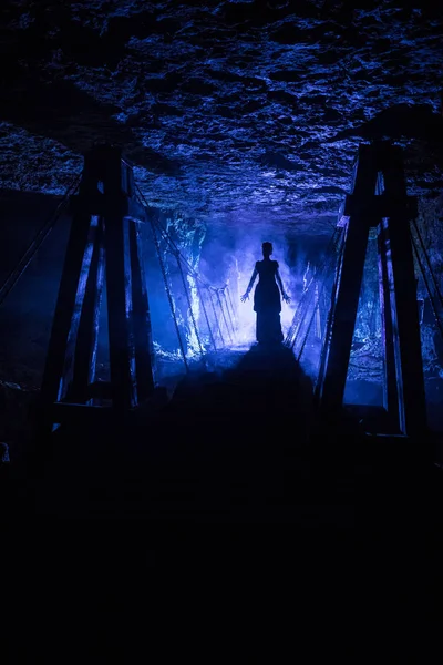 Silueta de una bruja misteriosa diciendo el hechizo y extendiendo sus manos a nosotros, con nubes de humo a su alrededor, y el puente de la mazmorra en el fondo — Foto de Stock