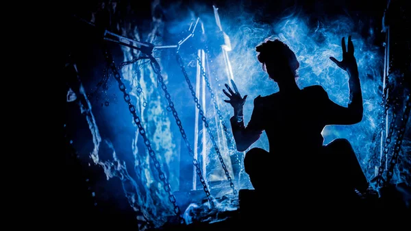 Silhouette di una strega misteriosa che dice l'incantesimo e ci tende le mani, con nuvole di fumo intorno a lei, e ponte sotterraneo sullo sfondo — Foto Stock