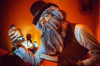 Sakallı adam bir elinde kitap ve başka bir şişe