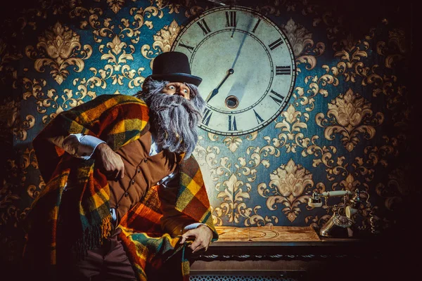 Hombre caucásico mayor de pie cerca de reloj de pared en la habitación oscura . — Foto de Stock
