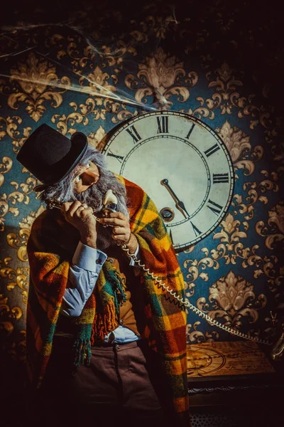 Senior caucasian man standing near wall clock in the dark room and talking on the phone. — Stock Photo, Image