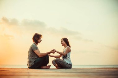 Genç çift gündoğumu arka plan üzerinde yoga yapıyor.