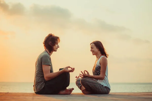 Pareja joven está haciendo yoga en el fondo del amanecer . — Foto de Stock