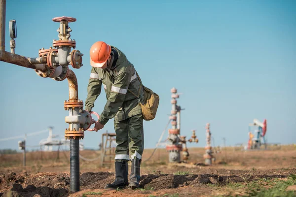 Ölarbeiter dreht Ventil an der Ölpipeline, Ölvorkommen im Hintergrund. — Stockfoto