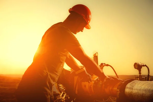 Il lavoratore petrolifero sta controllando la pompa dell'olio sullo sfondo del tramonto . — Foto Stock