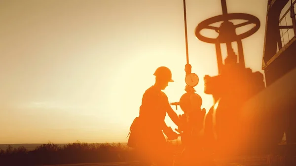 Ölarbeiter überprüft die Ölpumpe auf dem Hintergrund des Sonnenuntergangs. — Stockfoto