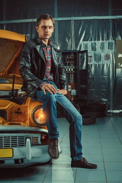 Motorista inteligente está sentado em seu carro velho na garagem — Fotografia de Stock