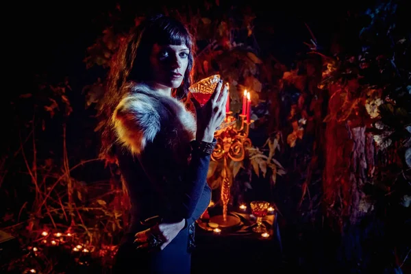 Beautiful witch with the glass of vine on the night forest background. — Stock Photo, Image